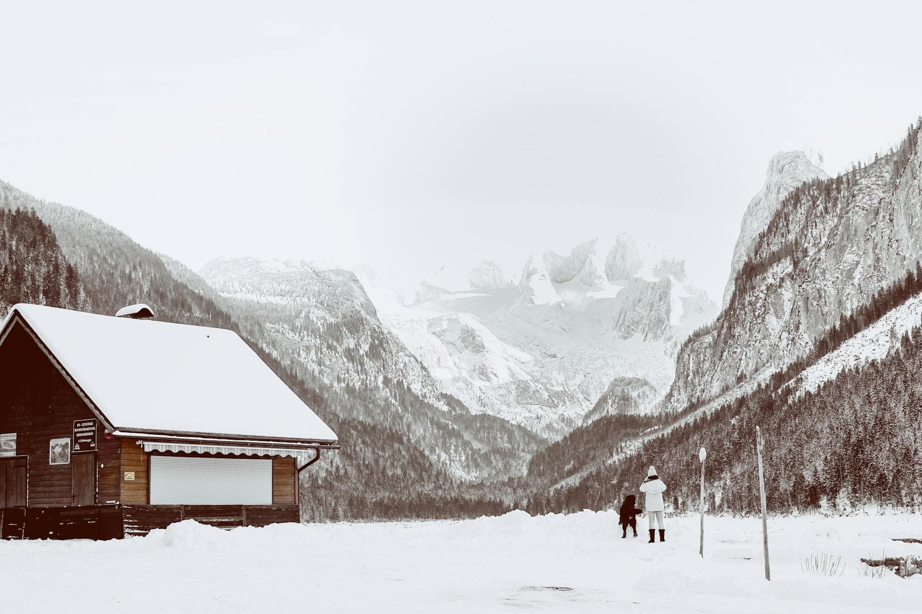 Un voyageur et son chien devant un chalet, vallée enneigée